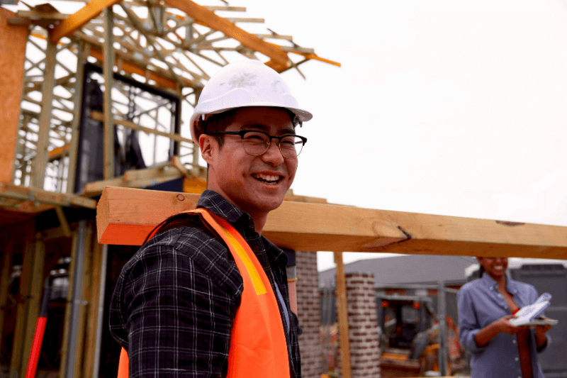 A light industrial staffing solutions hire in a hardhat and safety vest smiles at the jobsite.