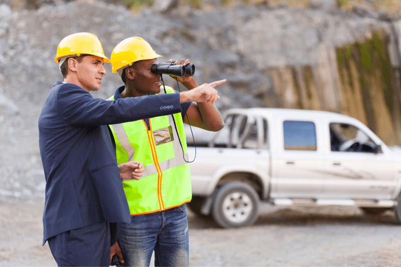 A mining recruitment expert uses binoculars while a site manager points and discusses the jobsite.